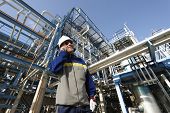 stock photo of construction  - refinery worker talking in phone with large pipeline construction in the background - JPG 