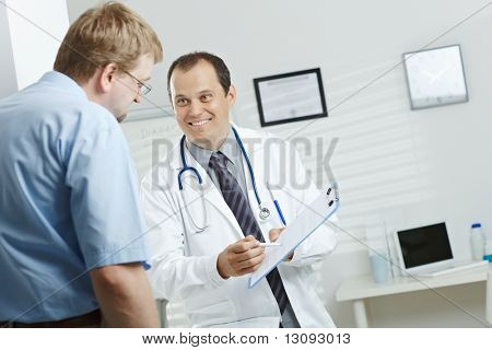 Picture or Photo of Medical office - smiling male doctor telling good news, explaining diagnosis on clipboard to happy patient.