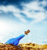 image of tilting  - Blue glass bottle in sand and airy clouds like genie - JPG 