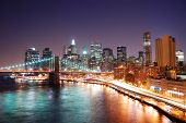stock photo of bridge  - New York City Manhattan skyline and Brooklyn Bridge with skyscrapers over Hudson River illuminated with lights and busy traffic at dusk after sunset - JPG 