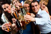stock photo of people  - Young people in club or bar drinking beer out of a beer bottle and have fun - JPG 