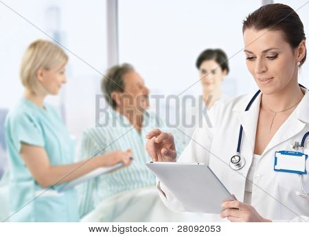 Picture or Photo of Doctor recording information to electronic tablet at patients bed, team working in background.?