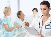 stock photo of information  - Doctor recording information to electronic tablet at patients bed - JPG 