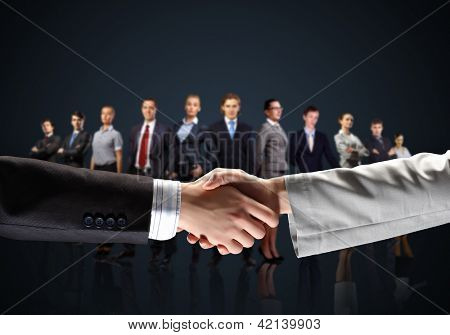 Picture or Photo of Business handshake against black background and standing businesspeople
