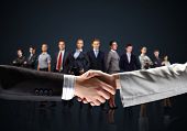 foto of meeting  - business handshake against black background and standing businesspeople - JPG 