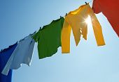 stock photo of on-line  - Colorful clothes hanging to dry on a laundry line and sun shining in the blue sky - JPG 