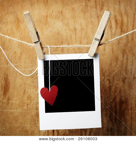 Picture or Photo of Blank instant photo and small red paper heart hanging on the clothesline. On dark grunge background.