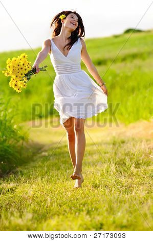 Picture or Photo of Candid skipping carefree adorable woman in field with flowers at summer sunset.