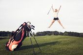 picture of golf  - Happy girl golfer jumping in the air with raised arms and golf club in hand after successful shot - JPG 