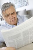 stock photo of newspaper  - Senior man reading newspaper with puzzled look - JPG 