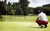 picture of golf  - Female golf player with putter squatting to analyze the green at golf course - JPG 
