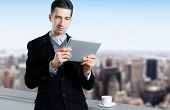 foto of businessmen  - Young businessman with a cup of coffee uses a digital tablet on the roof of business center - JPG 
