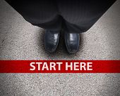 foto of business concept  - A business man is looking down at his feet with a red race line that says start here to represent a journey - JPG 