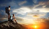 pic of sunset  - Two tourists with backpacks relaxing on top of a mountain and enjoying sunset view - JPG 