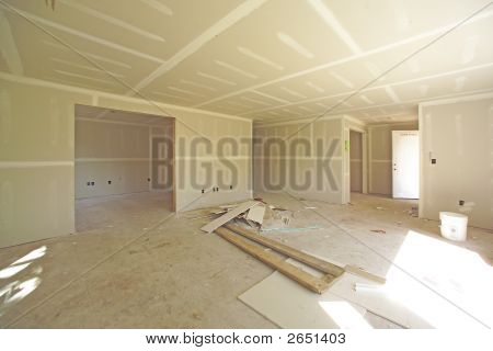 Picture or Photo of Image of house under construction showing unfinished surfaces and drywall implementation. This view is of living room looking into an extra room interior.