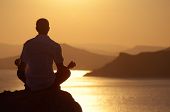 stock photo of sunset  - Guy meditating at sunset sitting on a rock by the sea - JPG 