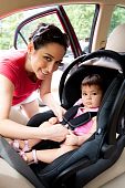 foto of seating  - Happy smiling mother placing baby in car seat and closing belt for safety - JPG 
