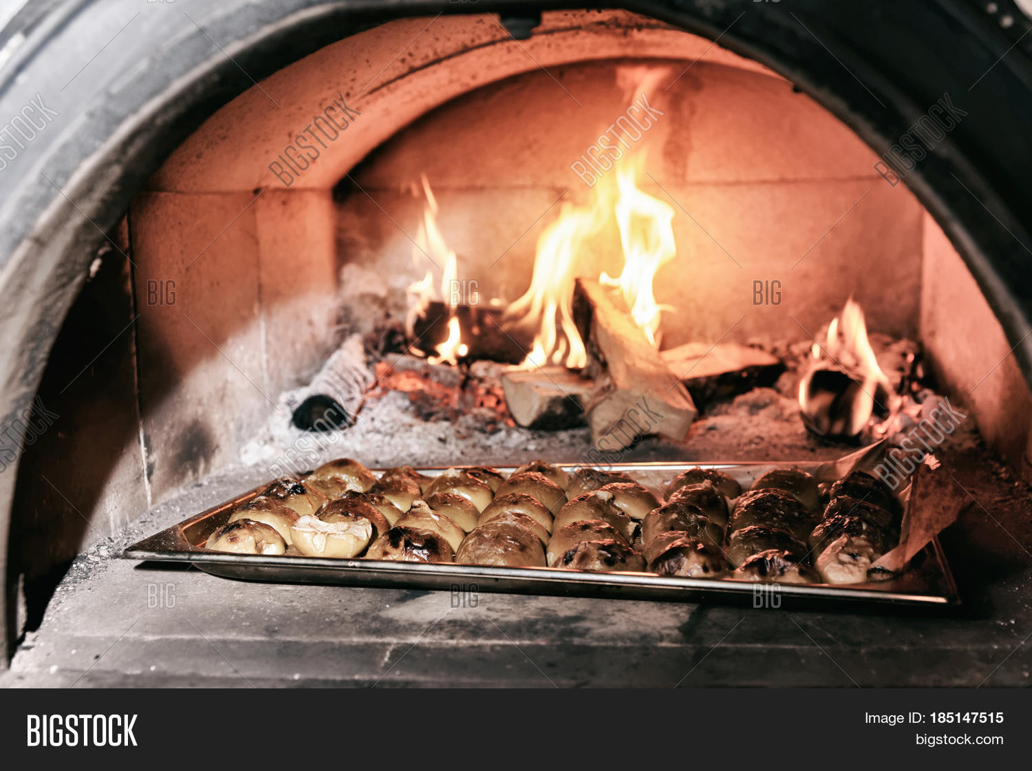 Apple halves being roasted in wood fired oven, professional kitchen of