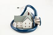 image of wrapped  - Blue stethoscope wrapped aroud tiny house model on white background - JPG 