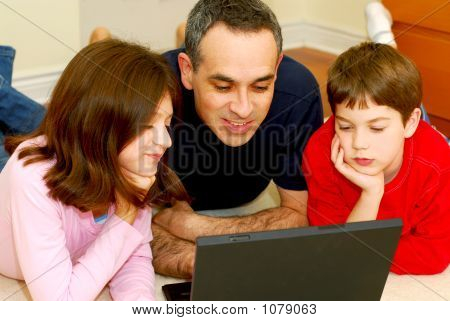 Picture or Photo of Father and children lying on the floor at home and looking into a portable computer
