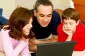 picture of computer technology  - father and children lying on the floor at home and looking into a portable computer - JPG 