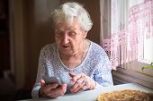 Elderly woman sits with a smartphone in her hands.