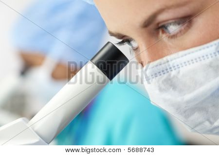 Picture or Photo of A female medical doctor or scientific researcher using her microscope in a laboratory with her colleague out of focus behind her.