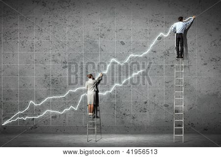 Picture or Photo of Businesspeople standing on ladder drawing diagrams and graphs on wall