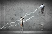 picture of competition  - businesspeople standing on ladder drawing diagrams and graphs on wall - JPG 