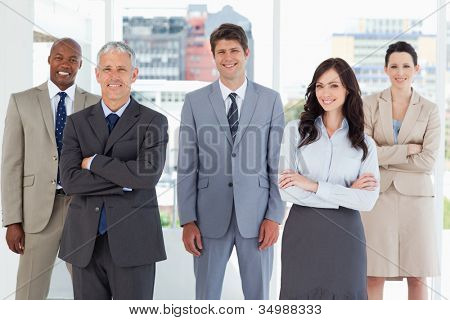 Picture or Photo of Young smiling executive standing in the middle of the room among his colleagues