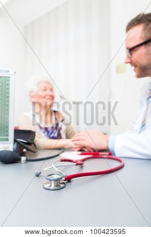Doctor sitting with pensioner in surgery consultation hour at desk