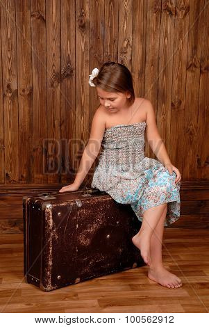 Smiling girl sits on the ancient brown scratched suitcase