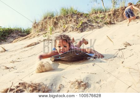 Young girl sliding down a sand dune on a sled in the summer. Some motion blur on girl and sand.