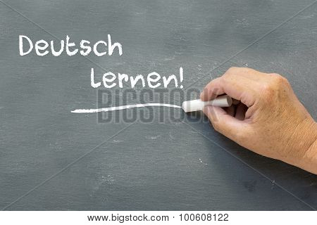 Hand On A Chalkboard With The German Words Deutsch Lernen (learning German)