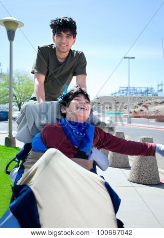 Big Brother Pushing Happy Disabled Boy In Wheelchair