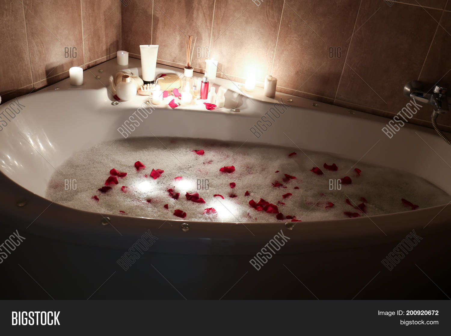 Spa accessories and candles on bathtub filled with foam and rose