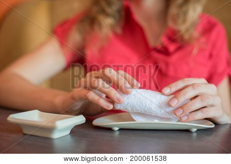 The girl wipes her hands with a hot white towel rolled into a roll in a Japanese restaurant before eating