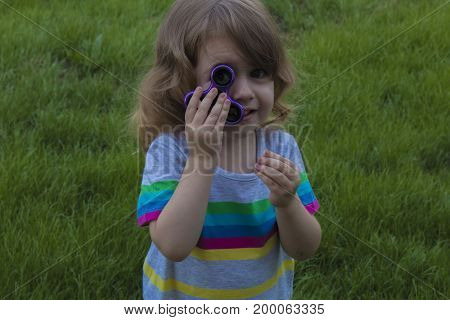 Little child is playing with the spinner lying on the green grass