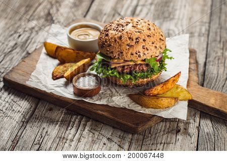 Cheeseburger served with sauce and French fries on cutting board