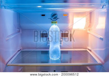 single cold water bottle on a shelf in refridgerator with warm light on good background for refreshing or healthy concept