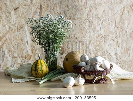 Still life with origano in a vase, pumpkins and a basket with mushrooms on a wooden table