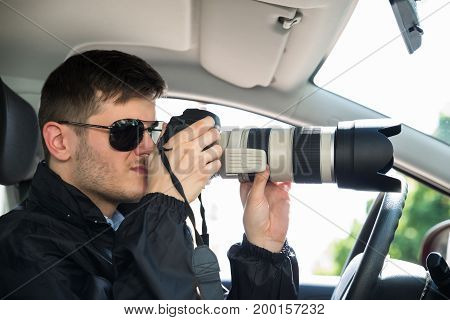 Side View Of A Private Detective Sitting Inside Car Photographing With Slr Camera