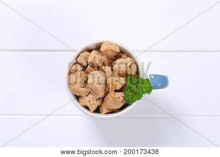 mug of soy meat cubes on white wooden background