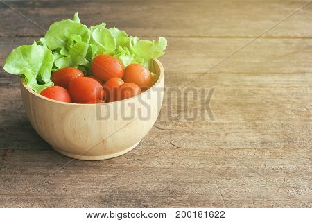 Fresh tomato and lettuce in wood bowl put on wood table. Side view close up of tomato and green oak lettuce with copy space for background. Fresh green oak lettuce and tomato prepare for cooking.