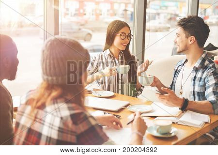 Lively communication. Positive smiling students drinking tea and sitting in the cafeteria while talking