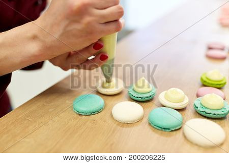 cooking, food and baking concept - chef with confectionery bag squeezing cream filling to macarons shells at pastry shop