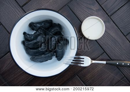 Close up bowl full of black dumplings traditional Russian dish with fork and sour cream