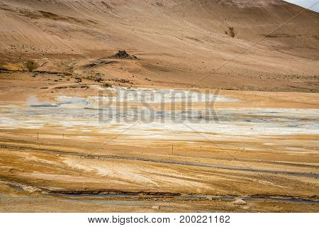 Mudpot in the Namafjall geothermal area, Iceland - area around boiling mud is multicolored and cracked.