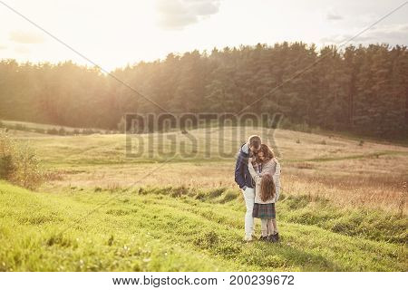 Lovely family of three members standing on green grass of meadow, embracing each other while feeling support and love. Small girl standing near her careful affectionate parents. Togetherness concept