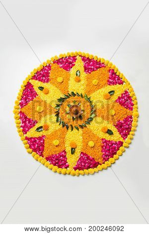 flower rangoli for Diwali or pongal made using marigold or zendu flowers and red rose petals over white background with diwali diya in the middle, selective focus